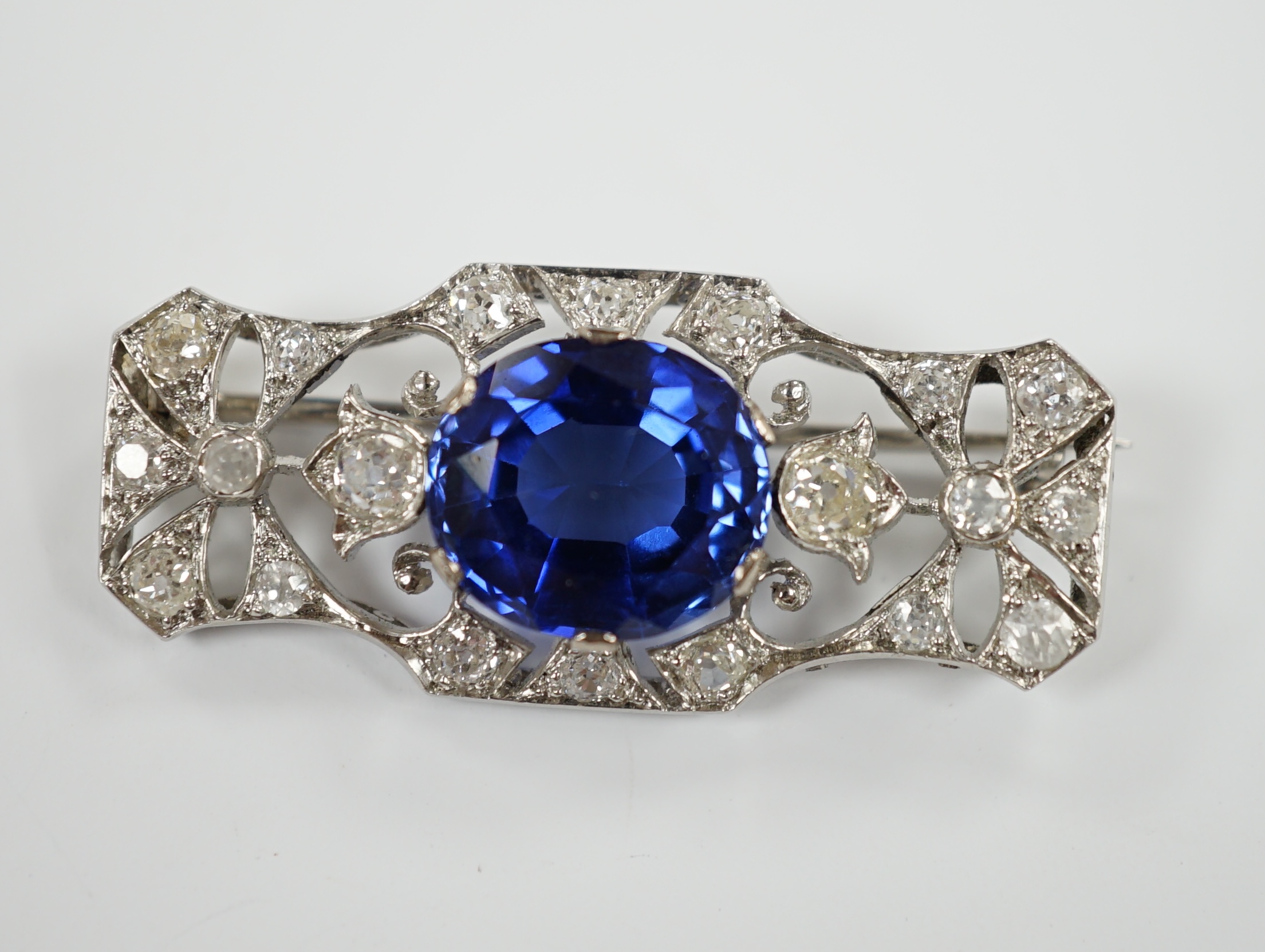 An Art Deco style pierced white metal, single stone synthetic sapphire and diamond cluster set shaped rectangular brooch, 36mm, gross weight 8.1 grams.